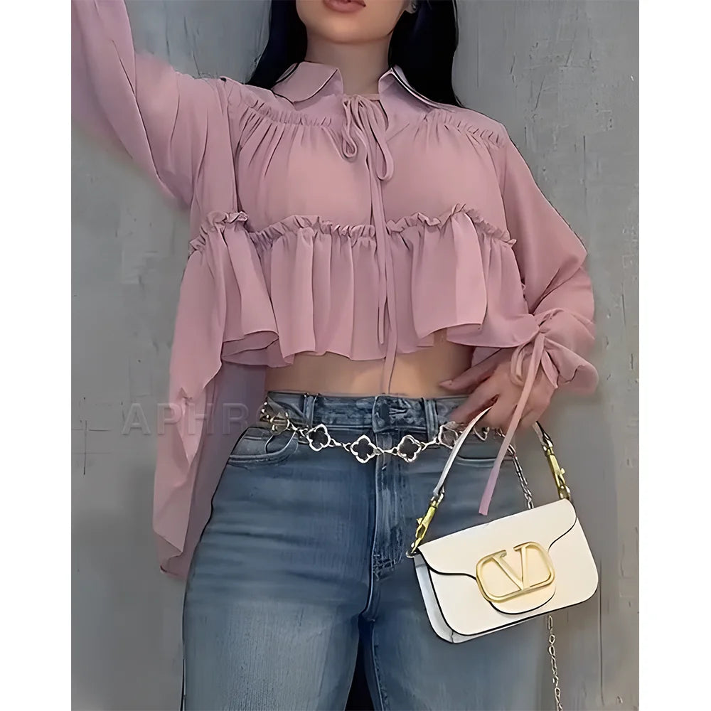 Person wearing a pink blouse and blue jeans, holding a white handbag with gold accents.